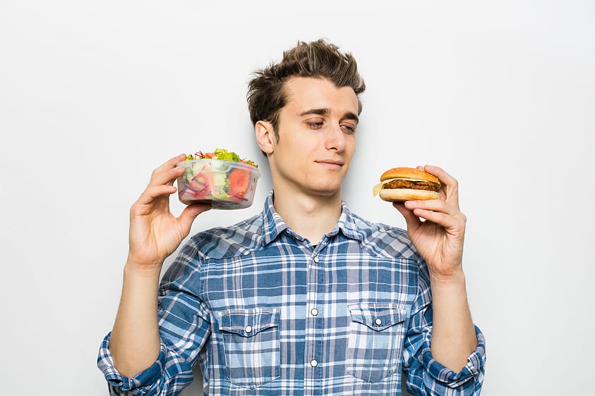 A man debates between a healthy and unhealthy food option