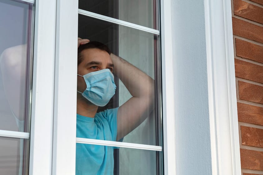 A man trying to detox at home wearing a mask looking at the window.