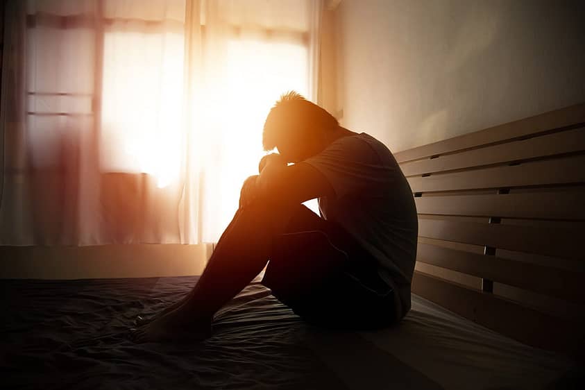 a person is curled up against a wall as sun streams through a window dealing with the negative effects of crack and cocaine abuse