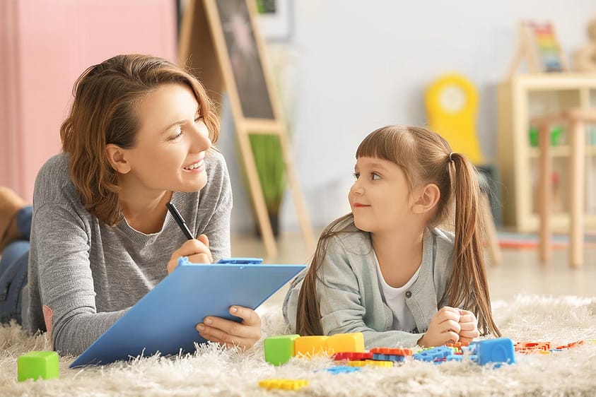 Mother smiles at daughter playing while considering the cost of play therapy.