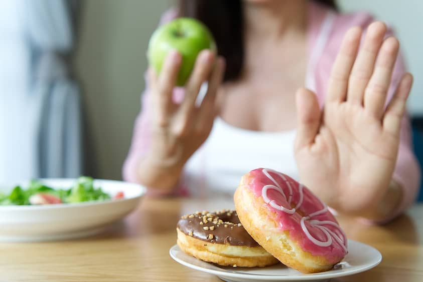 A woman rejects sugary treats like donuts for healthier alternatives like fruit and vegetables.