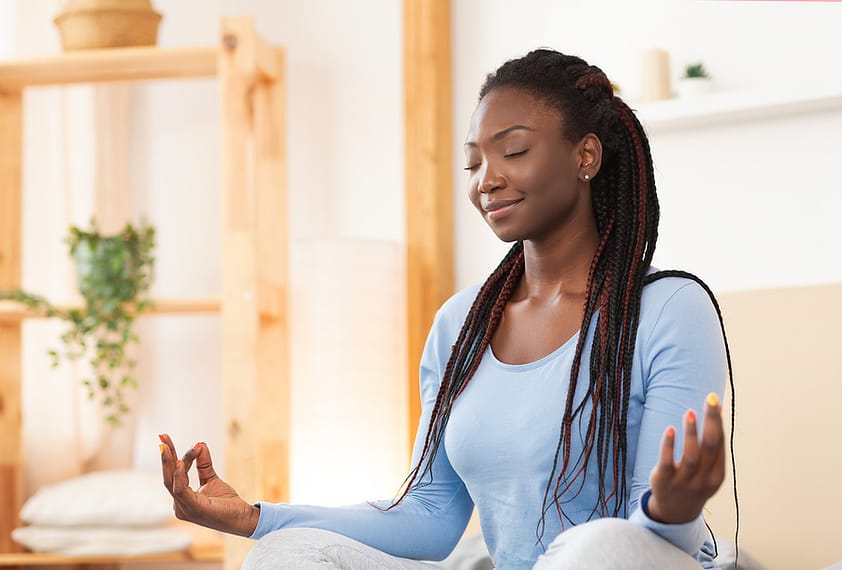 A woman smiling while she meditates at home.