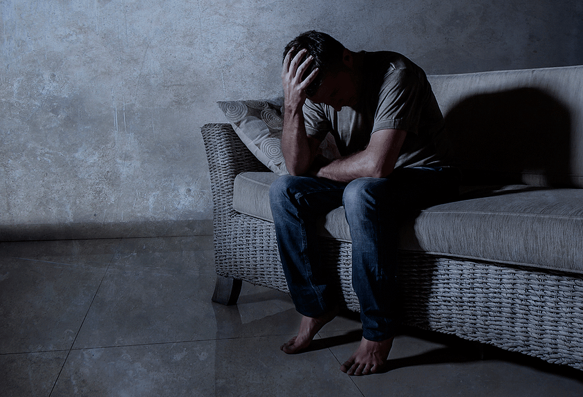 a young man holds his head in a dark room after recognizing he has signs of alcoholism in men