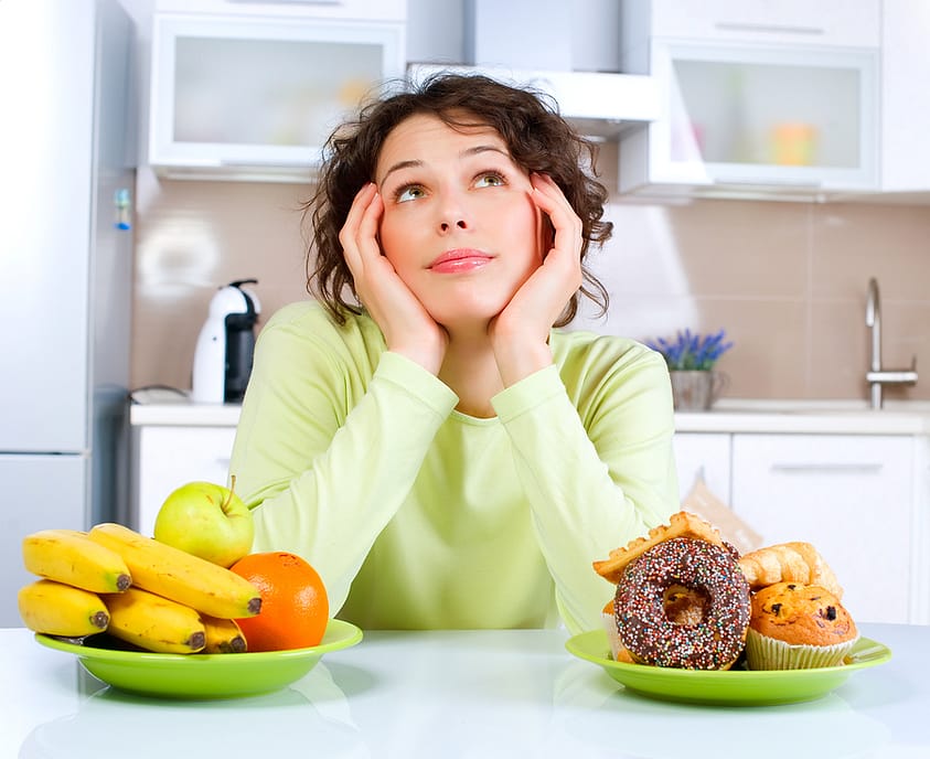 A young woman struggles to decide between healthy and unhealthy foods.