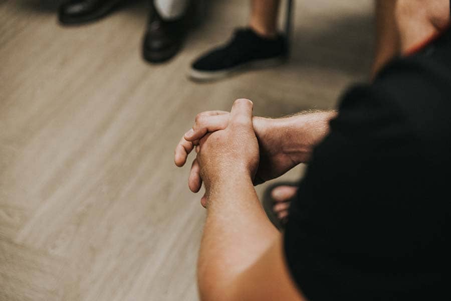 Patient with his fingers interlaced at an addiction treatment group therapy session