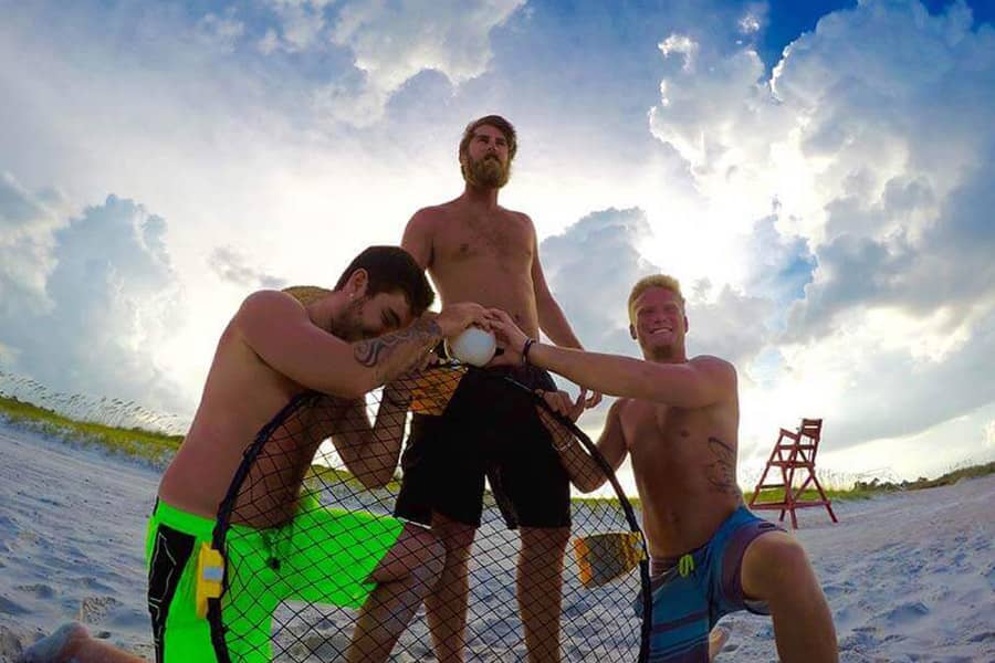 Three men playing handball on the beach